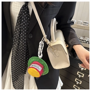 Close-up of a mini hat-shaped colorful pouch pendant with a carabiner on a beige handbag