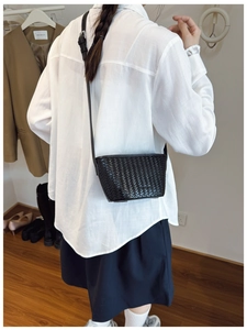 Detail view of black woven leather crossbody bucket bag worn with a white shirt and skirt