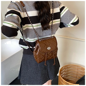 Detail of quilted dark brown leather backpack featuring silver twist lock and chain strap