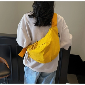 Detail of a vibrant yellow dumpling crossbody bag showing woven rope zipper and brand tag
