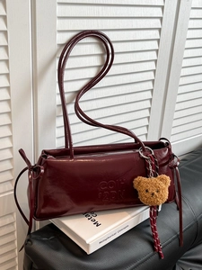 Retro burgundy patent leather shoulder bag with plush bear charm on white book