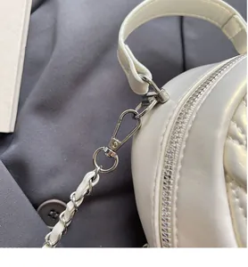 Close-up of durable silver metal hook and woven leather chain strap on white quilted backpack
