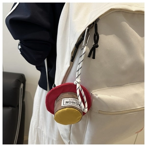 Mini round tricolor earphone pouch with snap hook hanging on a white backpack