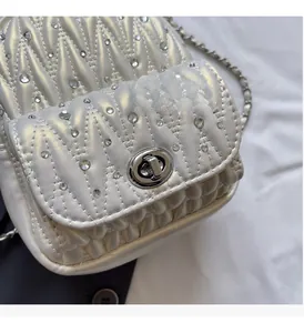 Detail of pearlescent white matelassé mini bag featuring silver twist lock and rhinestones