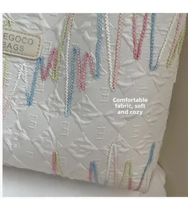 Macro shot of white quilted fabric with colorful wavy embroidery and leather brand tag