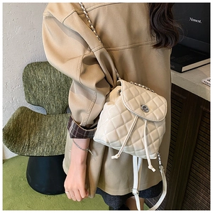 Quilted cream backpack featuring a metal chain strap and twist-lock on a model