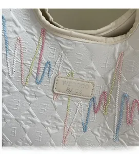Macro detail of quilted white tote bag with colorful wavy embroidery and brand label