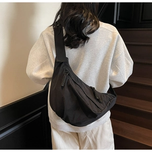 Detail view of black crescent crossbody bag featuring woven rope zipper and adjustable strap