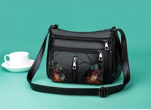 Detail of black faux leather crossbody bag featuring floral embroidery and multi-zipper layers