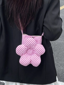 Sac bandoulière en forme de fleur à carreaux rose porté avec une veste noire chic