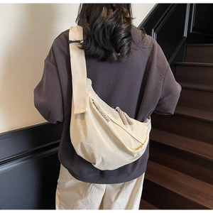 Detail of light beige crescent crossbody bag featuring woven zipper pull and wide strap