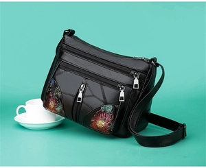 Close-up of black leather crossbody bag with floral embossed patterns and multi-zipper detail