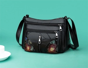 Detail of black crossbody bag featuring floral prints and multiple zipper compartments