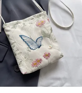 Detail of white crossbody bag with delicate blue butterfly and pink floral embroidery
