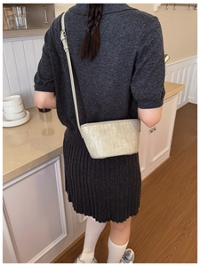Detail of woven beige bucket bag texture and logo during crossbody wear on a model