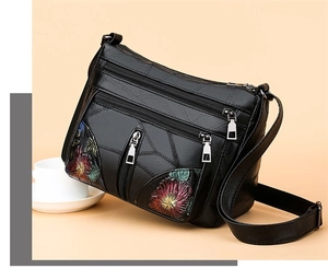 Close-up of black leather crossbody bag with vintage floral embroidery and zipper detail