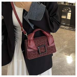 Detail of burgundy animal print handbag with matte black buckle and knot handle decor