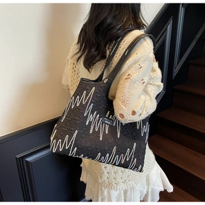 Detail of black tote bag featuring colorful wavy embroidery and textured fabric finish