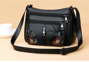 Macro detail of multi-layered zipper compartments and floral embroidery on black PU bag