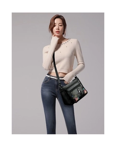 Detailed view of black faux leather crossbody bag featuring intricate floral embroidery