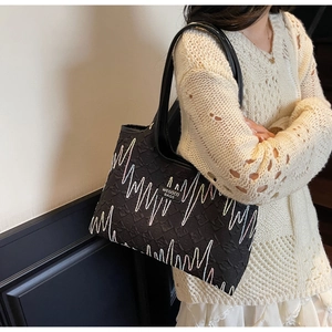 Detail of black tote bag featuring rainbow embroidery and embossed letter texture