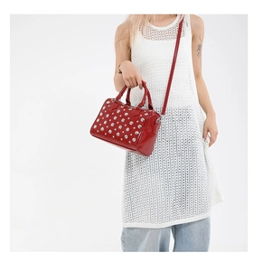 Detail of red glossy Boston bag featuring silver rivets and adjustable shoulder strap