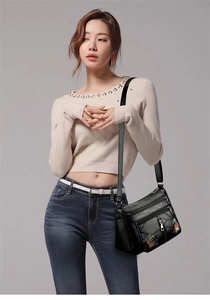 Detail of black faux leather shoulder bag featuring multi-zipper pockets and floral embroidery