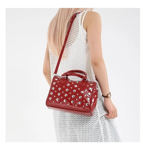 Glossy red patent leather bag with silver metal studs shown on shoulder