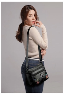Detailed view of black faux leather crossbody bag with colorful floral embroidery and zippers