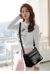 Detail of black soft leather crossbody bag featuring colorful floral embroidery and zippers