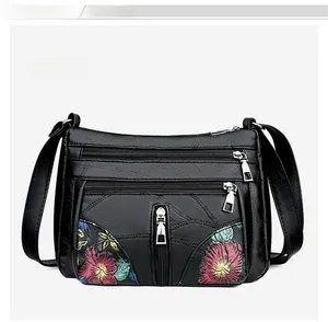 Detail of black faux leather shoulder bag with colorful floral embroidery and zippers