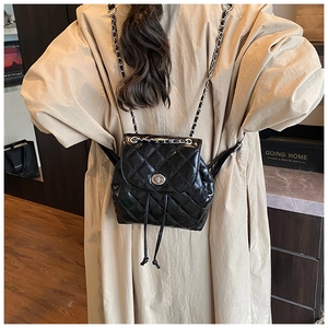Rear view of a model wearing a black quilted mini backpack with silver chain straps