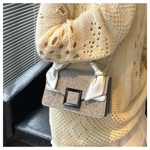 Detail of leopard print crossbody bag featuring a large black buckle and silver knot handle