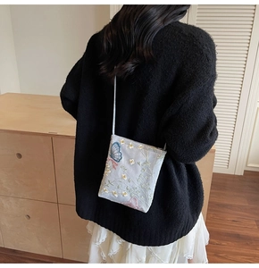Detail of light blue crossbody bag with pink butterfly and white floral embroidery