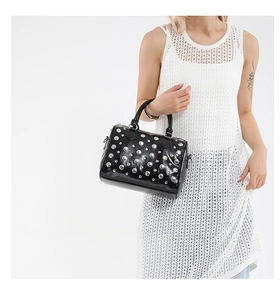 Detail shot of black pillow bag with silver rivets held by a model in a white dress