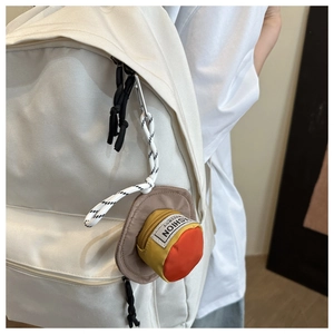 Detail view of mini hat-shaped coin purse with metal carabiner on white canvas backpack