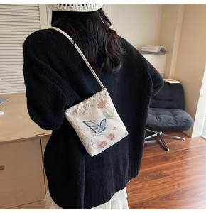 Detail of floral embroidery and blue butterfly pattern on a beige crossbody phone bag