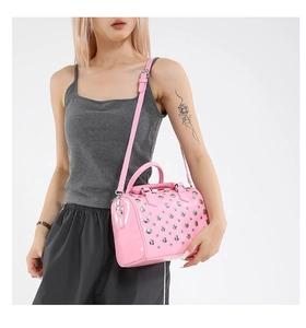 Pink patent leather boston bag with silver studs worn cross-body by a model