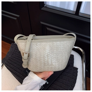 Close-up of beige woven bucket bag with adjustable strap and silver metal buckle