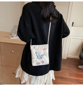 Close-up of elegant butterfly and floral embroidery on a white fabric crossbody bag