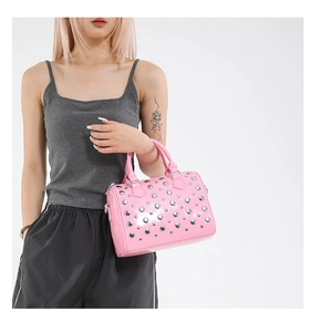 Detailed view of pink patent leather boston bag with silver studs on model's hand