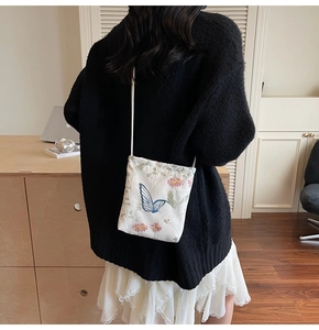 Detail of white crossbody bag with delicate blue butterfly and floral embroidery