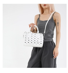 Close-up of white punk-style bucket bag featuring silver rivet studs and a detachable strap