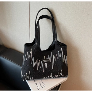 Detail of black quilted tote bag featuring vibrant zigzag stitching and brand logo patch