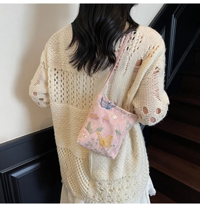 Detail view of pink embroidered crossbody bag with butterfly patterns on a model's shoulder