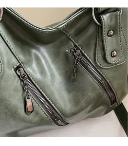 Dettaglio borsa in pelle verde scuro con cerniere diagonali e minuterie metalliche