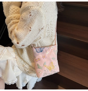 Close-up of pink embroidered phone bag with floral butterfly patterns on a white outfit