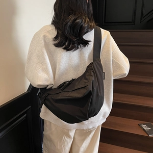 Minimalist black nylon dumpling bag with woven zipper pull worn by model on stairs