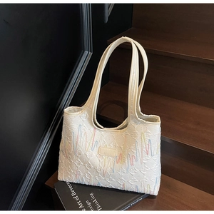 Detailed close-up of cream tote bag with colorful wave embroidery on textured logo fabric
