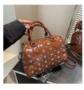 Detail shot of brown Boston bag with silver rivets and dual handles on black surface